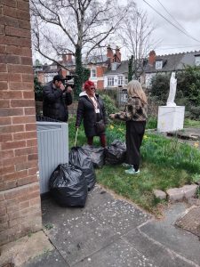 A man filming two women talking outside the Anawim centre. There are bags of cans around them.