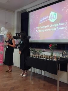 Two women in front of a stage presenting awards. 